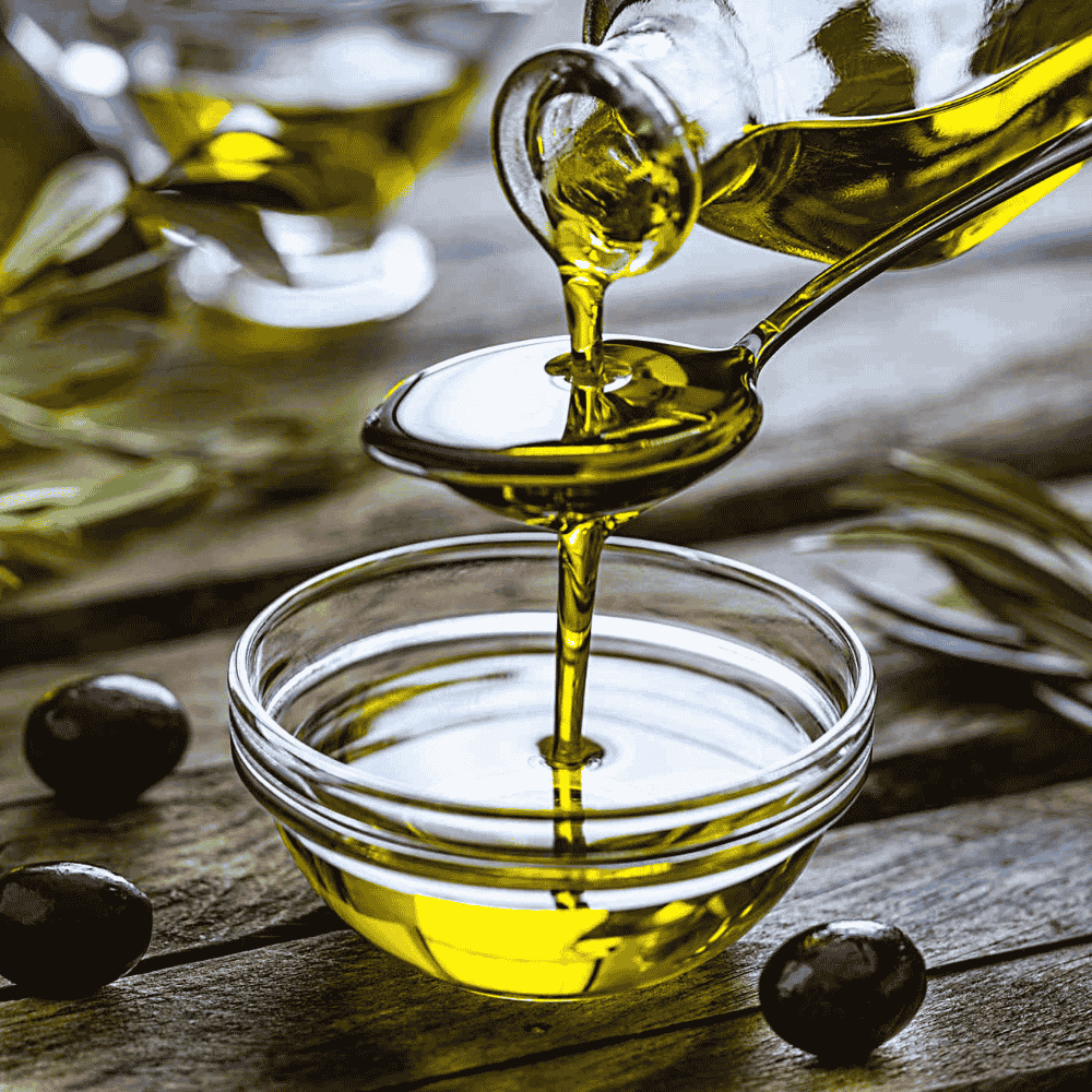 Olive oil being poured from a bottle into a glass bowl on a wooden surface.
