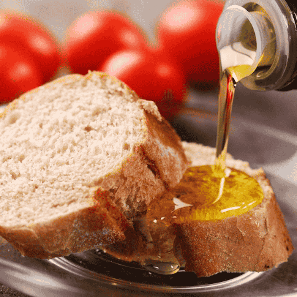 Olive oil being poured onto a slice of bread with tomatoes in the background