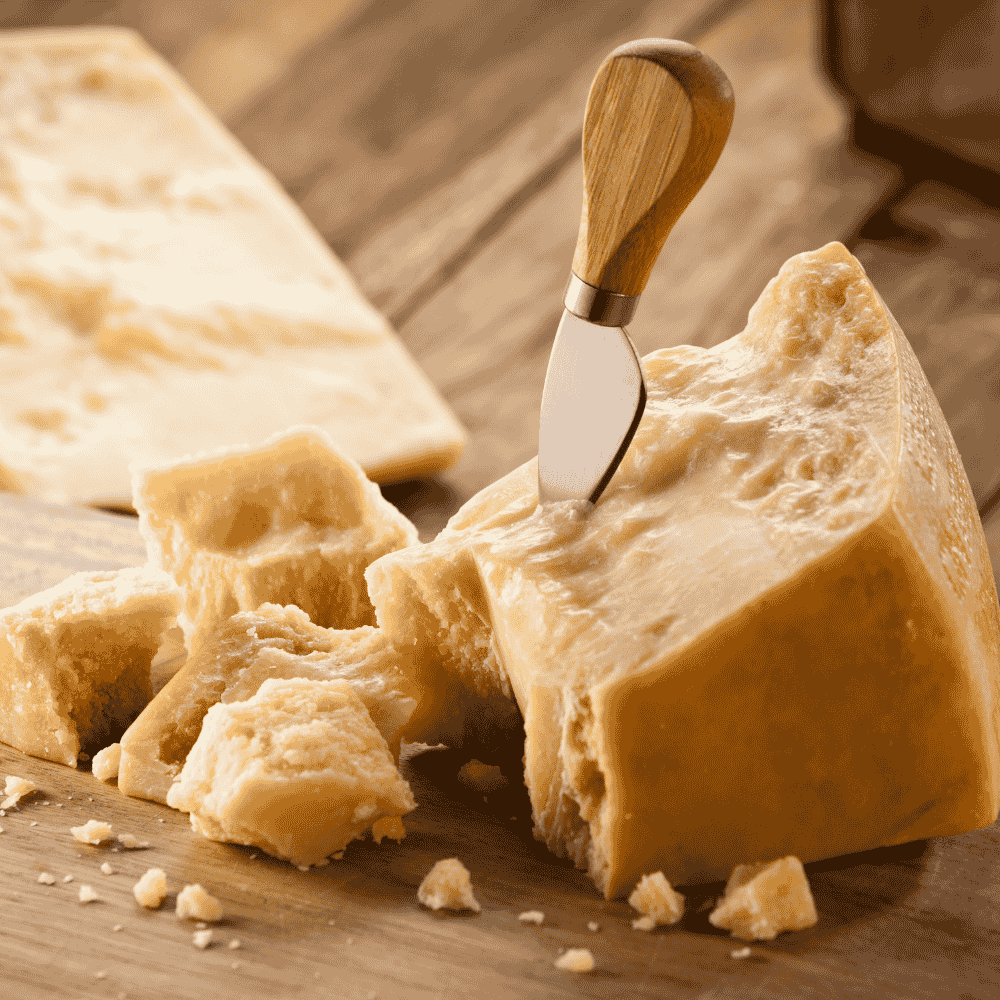Block of Parmesan cheese with a wooden-handled knife on a wooden surface