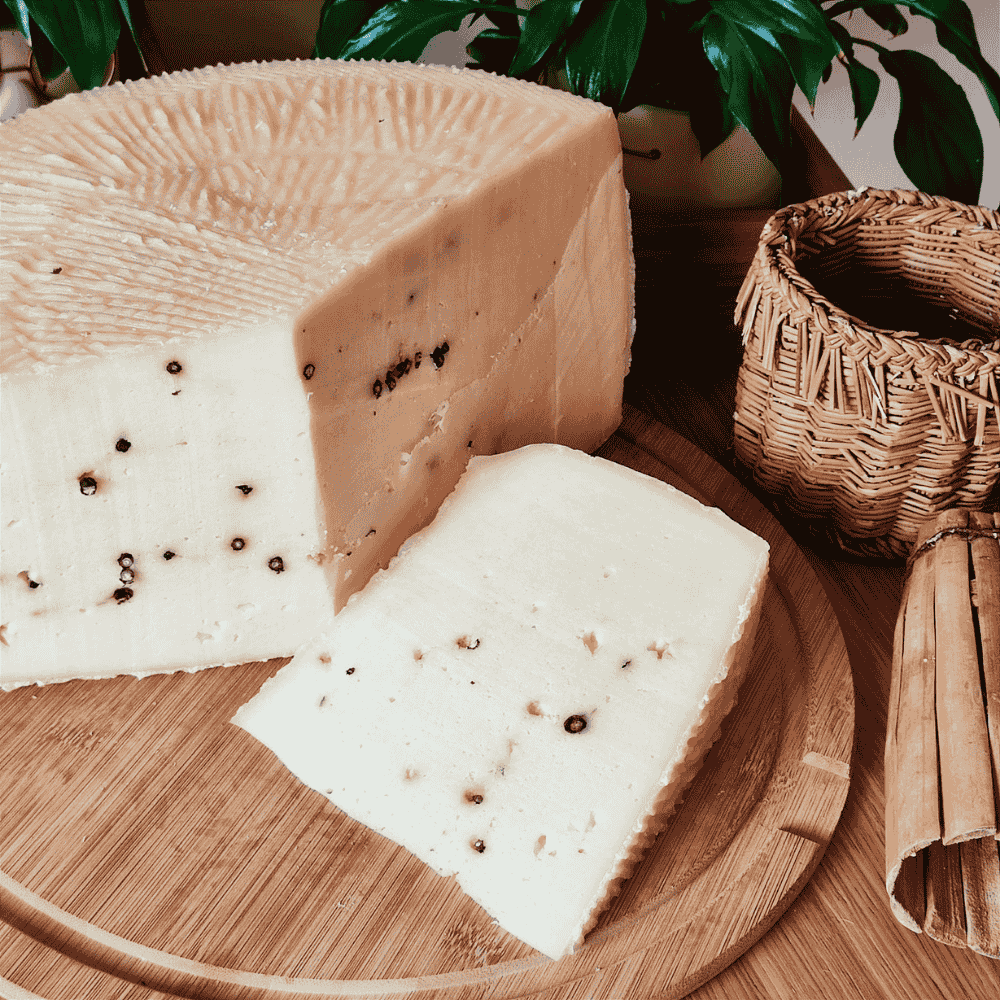pecorino with black pepper cheese on a wooden board with a plant and basket in the background